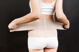 A cinta pós-cirúrgica na abdominoplastia é um cuidado importante que as pacientes precisam tomar logo após realizar essa cirurgia na barriga. O papel da cinta é ajudar na recuperação, por outro lado, não usá-la adequadamente pode envolver certos riscos. Saiba mais aqui. Usar a cinta pós-cirúrgica na abdominoplastia é imprescindível Um pós-cirúrgico bem cumprido é um dos primeiros passos para que a abdominoplastia seja bem-sucedida. Afinal, quando a paciente faz uma cirurgia para diminuir a circunferência abdominal e deixar a região mais reta e com a pele firme, ela quer ver esses resultados assim que possível. Entre os cuidados que devem ser tomados após realizar uma cirurgia de abdominoplastia e miniabdominoplastia está o repouso e o uso de uma cinta ou faixa abdominal pós-cirúrgica ininterruptamente, retirando apenas para o banho. As cintas mais conhecidas de tecido elástico compressivo são de lycra ou cetinete. Há diversos tipos de acessório, inclusive a cinta abdominal que só pega na cintura, ou camisete, body, bermuda e as placas de contenção. Quais são as principais funções da cinta pós-abdominoplastia? O uso desse acessório será imprescindível para atingir os resultados desejados pela paciente, porque garante uma sustentação dos músculos do abdômen e do seu entorno. Além disso, o acessório também modela a região. A cinta pós-cirúrgica abdominoplastia vai proteger a área operada e promover uma pressão no local da cirurgia, permitindo uma fixação da pele, facilitando a cicatrização das incisões, dando segurança e postura à paciente que está se recuperando. Com o uso da cinta, a paciente vai conseguir ficar com a coluna ereta, evitando que a barriga fique projetada para frente e também forme uma corcunda. Entre outras vantagens do uso do acessório está também conter a dor e os edemas (inchaços), que são muito comuns no pós-operatório. Além disso, o uso da cinta para abdominoplastia também vai combater a flacidez. No entanto, esse acessório tem algumas regras de uso que são gerais para a maioria dos cirurgiões plásticos, com alguma variação que pode envolver o tipo de técnica utilizada na cirurgia: Compressão e modelo A compressão da cinta e o modelo devem ser sempre orientados pelo cirurgião plástico, mas uma regra é que o acessório deve ser usado para provocar uma contenção uniforme da região operada, e não comprimi-la de forma exagerada. Além disso, quando a paciente for comprar a cinta, o melhor é experimentá-la para verificar se está no ajuste correto e se está confortável em todas as áreas do corpo, inclusive no que se refere à cinta pós-cirúrgica abdominoplastia e mamoplastia . Não caia no equívoco de comprar uma cinta menor, pensando já nas medidas que serão perdidas na abdominoplastia. Logo nos primeiros dias do pós-operatório, muitas pacientes podem sofrer inchaços progressivos, e uma cinta apertada demais vai se tornar insuportável para o uso. Uso com as placas O uso da cinta pós-cirúrgica abdominoplastia pode ser combinada às placas pós-cirúrgicas que, normalmente, são indicadas para evitar que a cinta dobre e a paciente sofra o garroteamento da região operada, que poderá trazer consequências definitivas para essa área, como as marcas que podem não sair mais. Assim, a placa vai proteger ainda mais a região. Tempo de uso As cintas pós-cirúrgicas, em geral, têm uma indicação de uso por 45 dias. Já as placas podem ser usadas por 30 dias. Esse tempo é o adequado para que o acessório contribua com a cicatrização dos tecidos no pós-operatório. No entanto, de acordo com a resposta inflamatória de cada paciente, o cirurgião poderá também indicar que, mesmo após esse período inicial de uso, a cinta seja retirada gradativamente, intercalando o uso em dias alternados. No entanto, após o período indicado pelo médico, a paciente não deve continuar usando a cinta com a intenção de modelar ainda mais o corpo. Essa atitude pode até prejudicar a assimetria abdominal, porque a compressão da cinta sobre os músculos vai impedir que eles se contraiam da forma natural adequada e causar enfraquecimento muscular na região. O que ocorre se a paciente não usar a cinta pós-cirúrgica abdominal ou fazer o uso errado? Como já citado mais acima, o uso da cinta cirúrgica na abdominoplastia traz uma diversidade de benefícios para as pacientes que querem um bom resultado no pós-operatório, enquanto não usá-las ou usar inadequadamente pode trazer consequências. O primeiro risco de não usar a cinta é a cicatrização mais lenta, e até mesmo a ocorrência mais facilmente de complicações pós-cirúrgicas, como sangramentos, infecções, abertura de pontos, etc. Além disso, o uso de uma cinta na compressão inadequada, além de promover muito desconforto e mais dor, pode até piorar a cicatrização e favorecer o surgimento de mais hematomas no abdômen e formação de líquidos, aumentando o inchaço, que já é comum no período pós-cirúrgico. Outro problema de uma cinta que está fazendo uma compressão exagerada é o prejuízo para a circulação sanguínea, especialmente para o retorno venoso dos membros inferiores, porque o acessório pode se tornar uma barreira na volta do sangue ao coração. Por isso, a cinta precisa estar na compressão correta tanto na região da barriga, como das virilhas e coxas. Outro ponto importante é que até mesmo a alça da cinta deve estar confortável, porque quando o acessório está muito apertado na região, os pacientes podem sofrer com cefaleias ou enxaquecas. Um conselho médico é que a paciente, especialmente nos primeiros dias do pós-operatório, não faça esforço para colocar a cinta. O melhor é pedir ajuda para outra pessoa porque o período exige repouso, e esse trabalho intenso para vestir a cinta pode até provocar tonturas e até desmaios. Cinta pós-cirúrgica abdominoplastia: preço A cinta pós-cirúrgica para abdominoplastia não costuma ser barata. Os valores aproximados, de acordo com o modelo, podem variar de R$ 400 a R$ 800 (*). Ainda que os preços sejam salgados, o ideal é comprar mais que uma cinta para os momentos de troca para lavar. Quando a paciente tira a cinta vai ficar um bom tempo sem o uso do acessório, com o abdômen solto, se não tiver outro modelo para vestir. Ficar sem essa proteção pode prejudicar o processo de cicatrização. Por isso, quando a paciente decide fazer uma cirurgia plástica, o planejamento financeiro também é importante, porque existem os custos de consultas, equipe médica, internação, cirurgia em si e até a aquisição desses acessórios, que também devem ser contabilizados. (*) Valores de julho de 2021.
